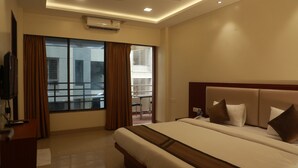 A hotel room with a large bed, a TV on a stand, a ceiling fan, and a window with curtains.