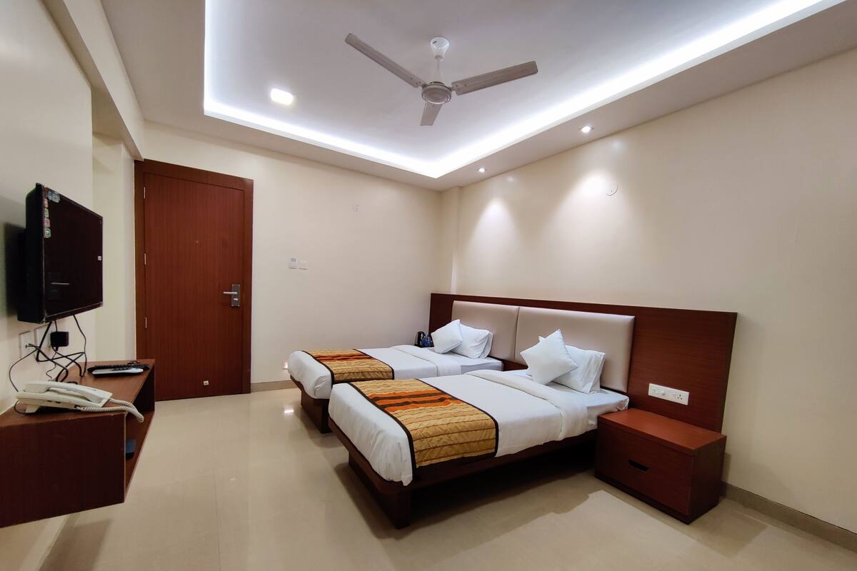 A hotel room with two beds, a ceiling fan, a TV, a telephone, and a wooden nightstand.