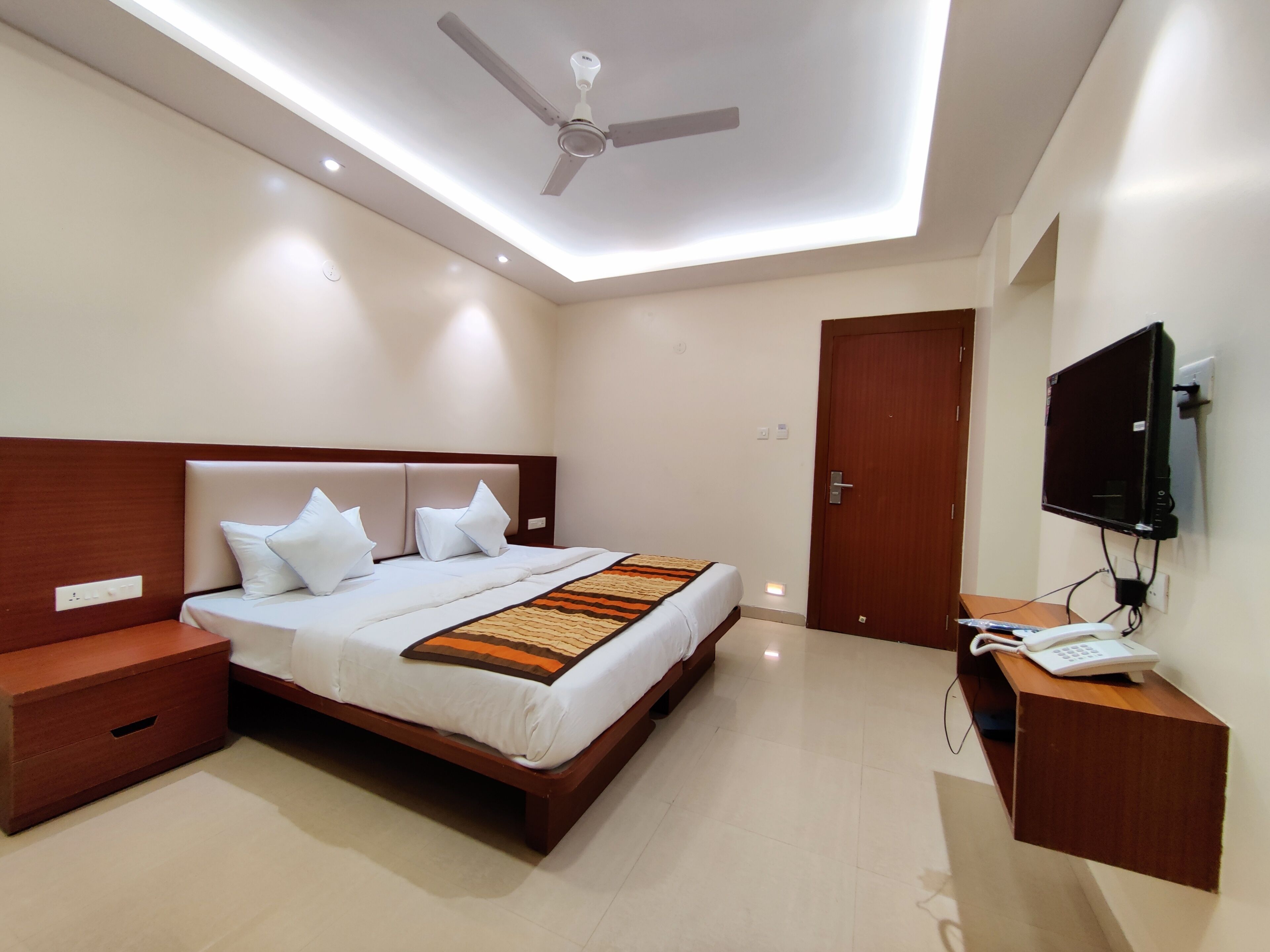 A modern bedroom with a bed, bedside tables, a ceiling fan, a TV, and a desk with a telephone.