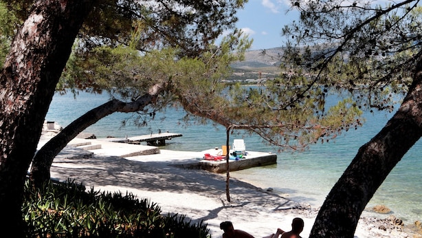 A lakeside area with a dock, a sandy beach, and two people relaxing on a beach towel. - Large Apartment w. big Terrace, Next to the Beach (Trogir)