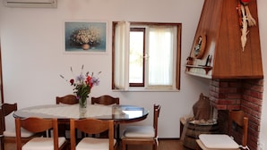 A dining area with a round table, six wooden chairs, a vase with flowers, a window with curtains, and a brick fireplace. - Large Apartment w. big Terrace, Next to the Beach (Trogir)