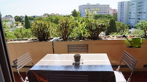 An outdoor patio with a table and chairs, a metal chair, and a green container. - Beautiful spacious and bright apartment with large balcony (Montpellier)
