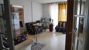 A modern living room with a sofa, armchairs, and a coffee table. There are potted plants and a bookshelf. - Beautiful spacious and bright apartment with large balcony (Montpellier)