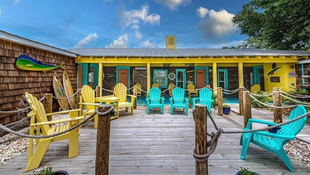 A wooden deck with yellow and turquoise Adirondack chairs, a wooden building with a yellow facade, and a clear blue sky.