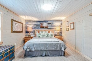 Quarto com teto de madeira, uma cama com colcha cinza, duas mesas de cabeceira com abajures e um ar condicionado fixado na parede.