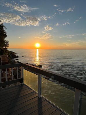 Une vue sur le coucher de soleil depuis une terrasse en bois donnant sur une mer calme.