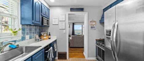 A kitchen with blue cabinets, stainless steel appliances, and a view to the living area.