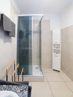 Ein modernes Badezimmer mit einer glasumrandeten Dusche, einer Holzbank und einem weißen Schrank.