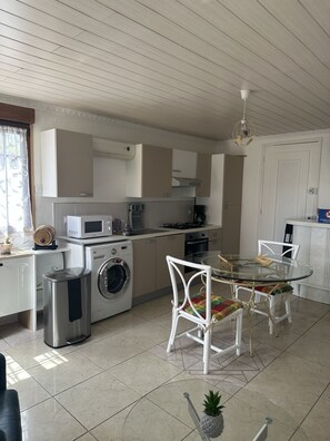 A modern kitchen with a dining area, including a washing machine, microwave, and a glass-top table with chairs. - The art of living combined with calm (Balloy)
