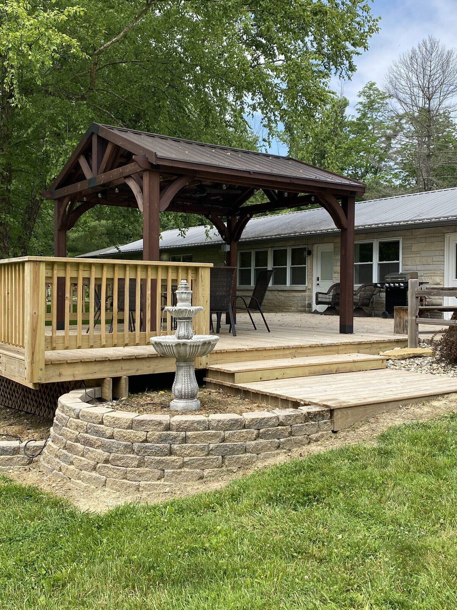 A wooden deck with a pergola, a stone fountain, and a barbecue grill.