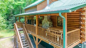 Eine Blockhütte mit Holzterrasse, Kamin aus Stein und überdachter Veranda.