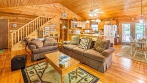 Ein gemütliches Blockhaus-Interieur mit Holzvertäfelung, einer Wendeltreppe, einem Wohnzimmer mit zwei Sofas, einem Essbereich und einer Küche.