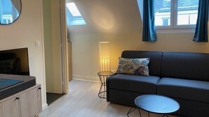 Een moderne woonkamer met een bank, een klein rond tafeltje, een lamp en een dakraam.