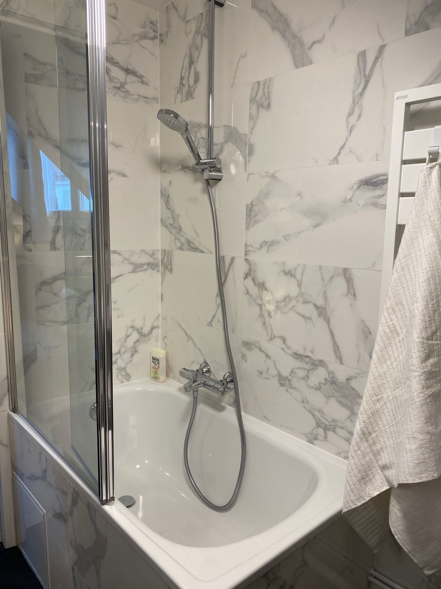 A bathroom with a glass-enclosed shower, a white bathtub, and marble-patterned walls.