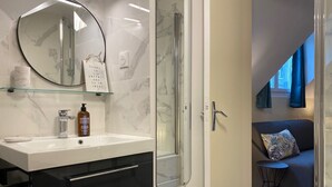 Een moderne badkamer met een douchecabine van glas, een witte wastafel met een marmeren aanrechtblad en een zwart badmeubel met lades.