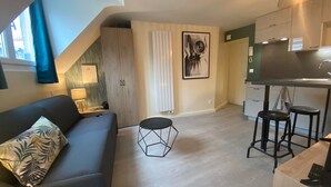 Een knus woongedeelte met een bank, een klein rond tafeltje, een kitchenette en een trap.
