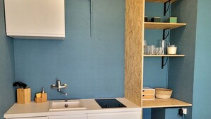 Eine kleine Küche mit Spüle, Schränken und einer Arbeitsplatte. Über der Spüle befinden sich Regale und ein kleines Fenster.