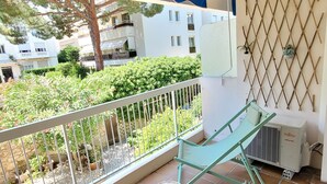 Ein Balkon mit Metallgeländer, einem grünen Stuhl, einem gewebten Hocker und einem blauen Sonnensegel.