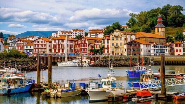 A harbor with boats docked, surrounded by colorful buildings with red and white facades. - Maisonnette de Charme (Arbonne)