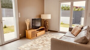 A living room with a sofa, a TV on a wooden stand, a lamp, and a patterned rug. - Maisonnette de Charme (Arbonne)