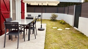 A patio with a table and chairs, a covered umbrella, and a small garden area with stepping stones. - Maisonnette de Charme (Arbonne)