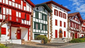 A row of traditional half-timbered houses with red and white facades, a clear sky, and parked cars. - Maisonnette de Charme (Arbonne)