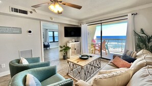 A living room with a ceiling fan, a television, and a view of the ocean through a sliding glass door. - Harbour Place 511 3 Bedroom Condo by RedAwning (Orange Beach)