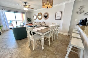 A dining area with a table and chairs, a ceiling fan, decorative wall mirrors, and a view of the outside. - Harbour Place 511 3 Bedroom Condo by RedAwning (Orange Beach)