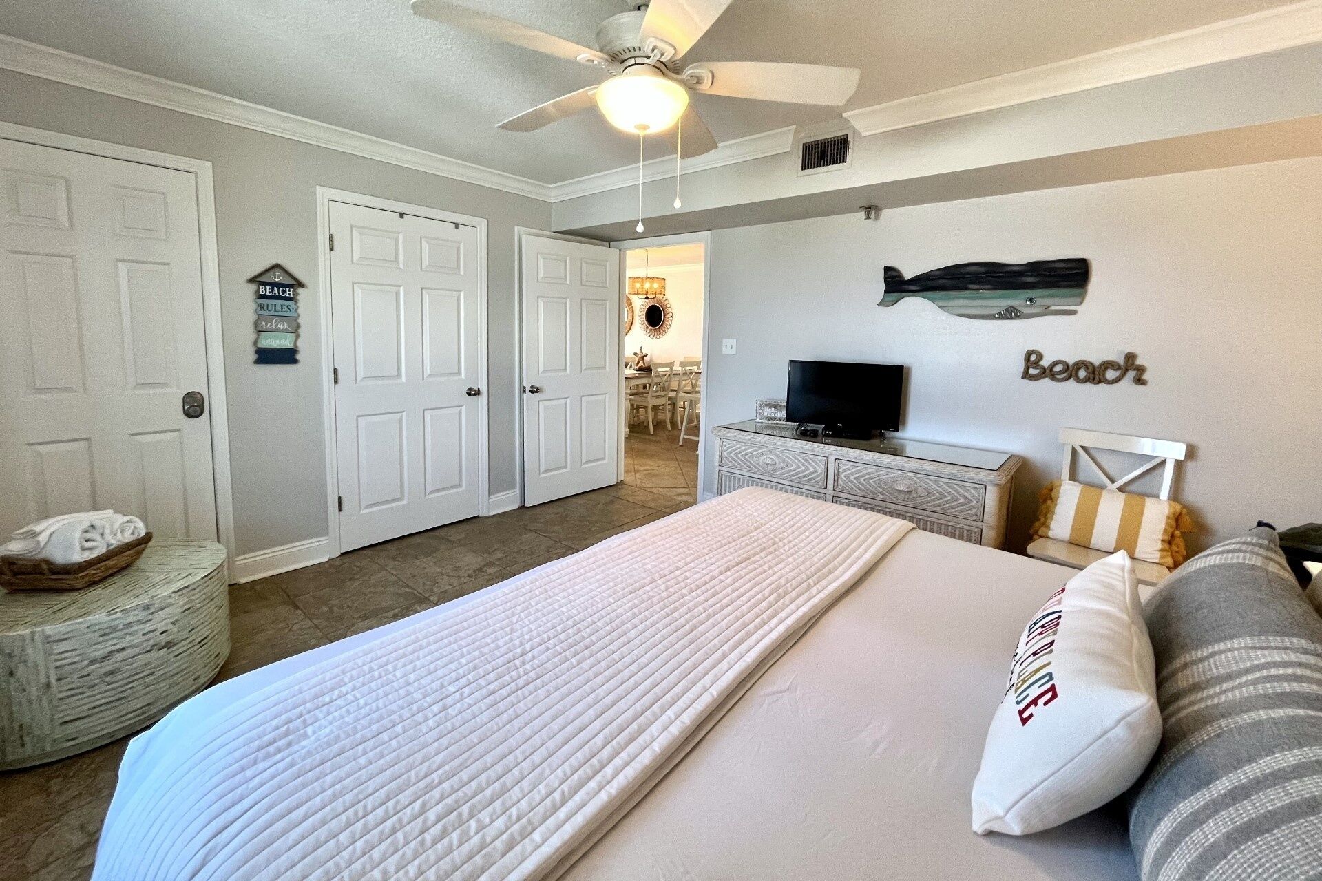 A bedroom with a bed, a television, and a ceiling fan. There are two doors and a small seating area with a table and chairs.
