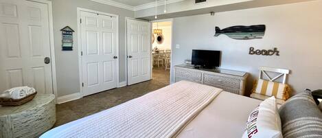 A bedroom with a bed, a television, and a ceiling fan. There are two doors and a small seating area with a table and chairs.