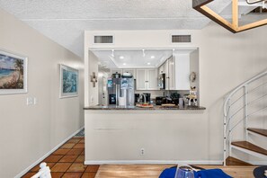 Una cocina con armarios blancos, una isla central y un comedor con mantel azul.