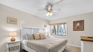 Un dormitorio con cama, mesitas de noche, ventilador de techo y ventana con persianas.