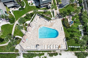 Ein Luftbild eines Schwimmbeckens mit umlaufender Liegefläche, Liegestühlen und einem kleinen Garten.