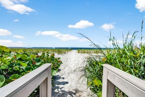Ein Sandweg am Strand, der zum Meer führt, mit einer Holzgeländer auf einer Seite.