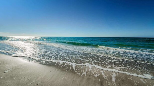 A beach with clear water, a sandy shore, and a clear sky.