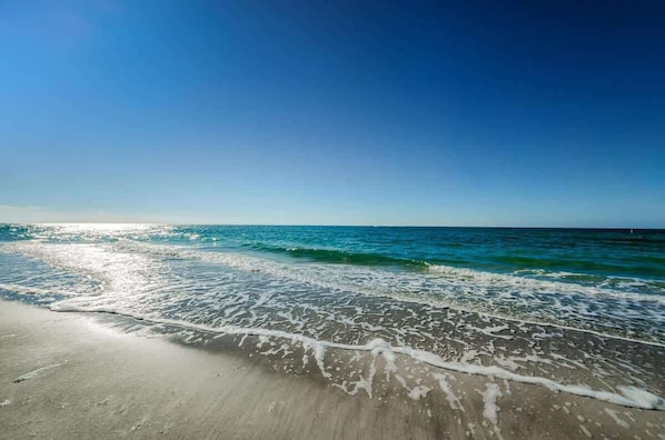 A beach with clear water, a sandy shore, and a clear sky.