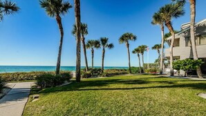 A beachfront property with a well-maintained lawn, palm trees, and a clear view of the ocean.