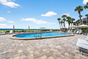 Una piscina con vista al océano, rodeada de palmeras y sillas de descanso.