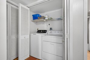 Una sala de lavandería con lavadora, secadora y estantes con productos de limpieza.