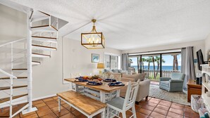 Un amplio salón con una mesa de comedor preparada para cuatro personas, un sofá y una escalera.
