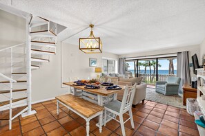 Un amplio salón con una mesa de comedor preparada para cuatro personas, un sofá y una escalera.