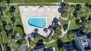 Vista aerea di un resort con piscina, palme e un viale lastricato.