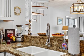 Una cocina moderna con encimeras de granito, un lavamanos, horno empotrado, licuadora y un reloj decorativo.