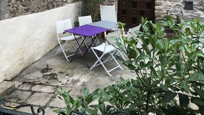 Un edificio de piedra con un pequeño patio que tiene una mesa morada y sillas blancas.