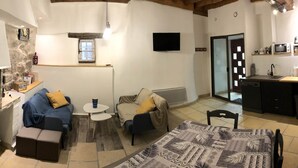 Una habitación acogedora con pared de piedra, chimenea, sofá, una mesita y una zona de cocina con microondas y fregadero.