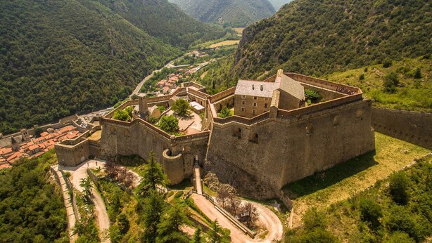 Vista aérea de un castillo histórico de piedra rodeado de abundante vegetación y un valle.