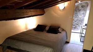 Un dormitorio con cama, vigas de madera, pared de piedra y una pequeña mesa.