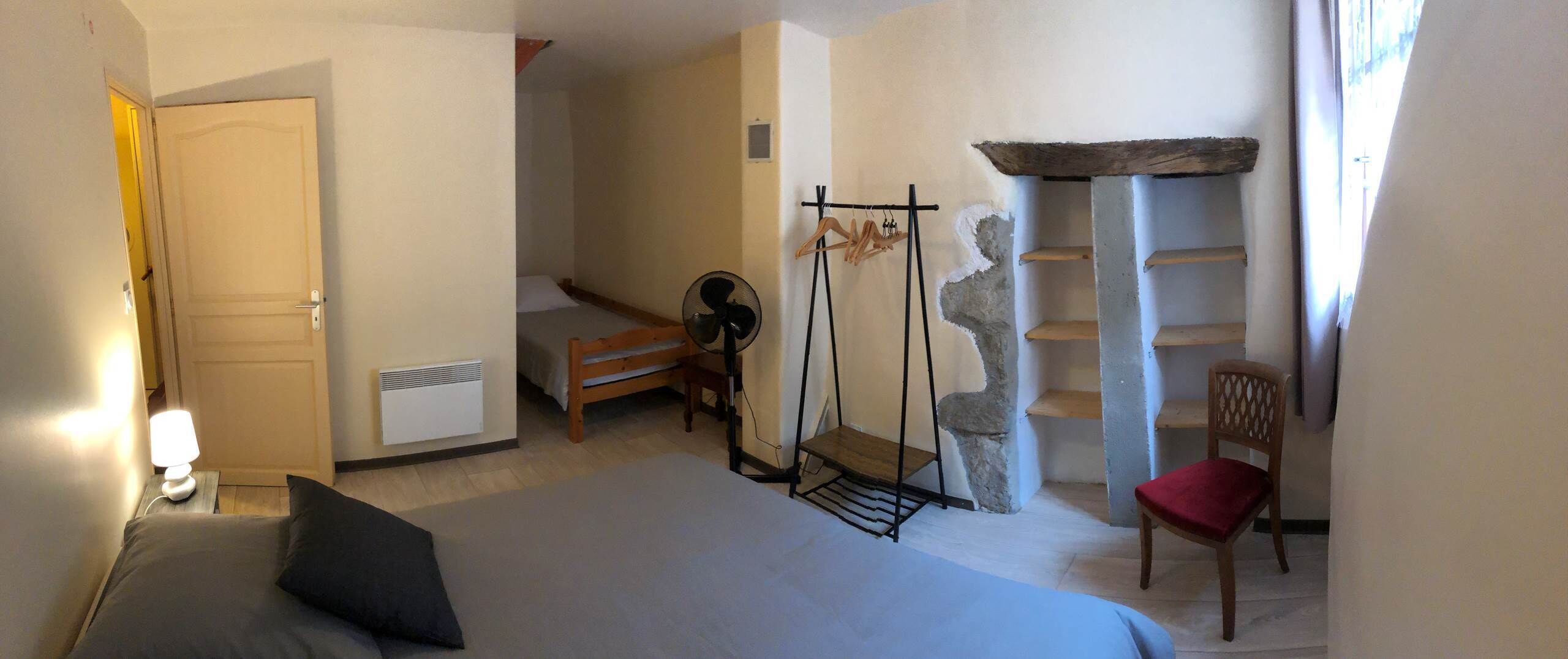 A bedroom with a bed, a chair, a fan, a heater, a coat rack, and a stone shelf.