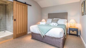 Ein Schlafzimmer mit einem großen Bett, zwei Nachttischen, einem Holzschrank und einer Schiebetür zu einem Duschbereich.