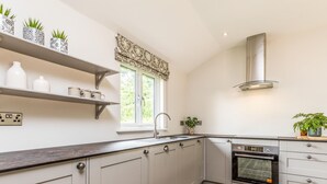 Una cocina moderna con armarios grises, encimera de madera, horno empotrado y ventana con vistas a zonas verdes.